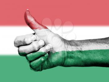 Old woman with arthritis giving the thumbs up sign, wrapped in flag pattern, Hungary