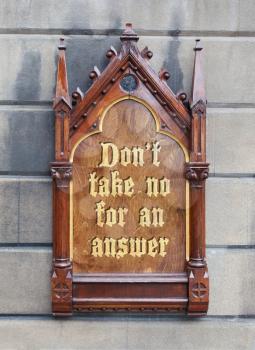 Decorative wooden sign hanging on a concrete wall - Don't take no for an answer
