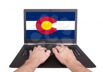 Hands working on laptop showing on the screen the flag of Colorado