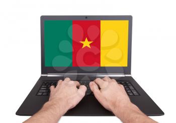 Hands working on laptop showing on the screen the flag of Cameroon