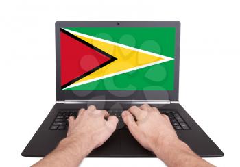 Hands working on laptop showing on the screen the flag of Guyana