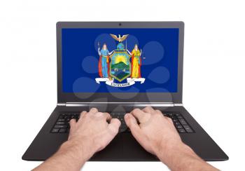 Hands working on laptop showing on the screen the flag of New York