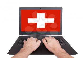 Hands working on laptop showing on the screen the flag of Switzerland