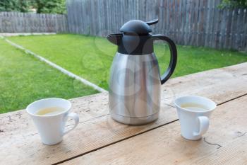 Thermos bottle with two mugs in a garden