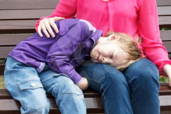 Mother with sleeping son has a rest on bench