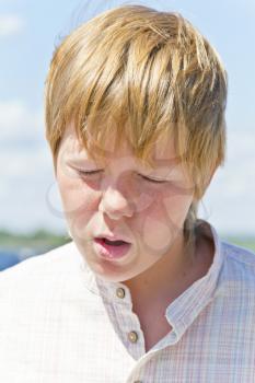 Portrait of squint blond boy in a white shirt near river