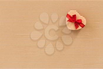 Heart shaped gift box with red ribbon and bow on corrugated cardboard background. 