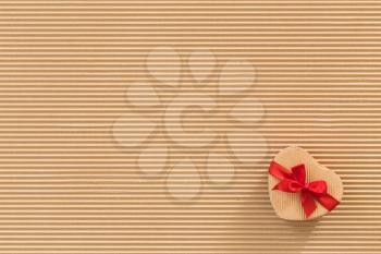 Heart shaped gift box with red ribbon and bow on corrugated cardboard background. 