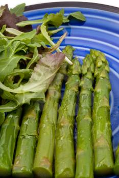 boiled green asparagus with salad mix on blue plate