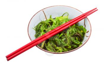 seaweed salad sprinkled with sesame seeds in bowl with red chopsticks isolated on white background