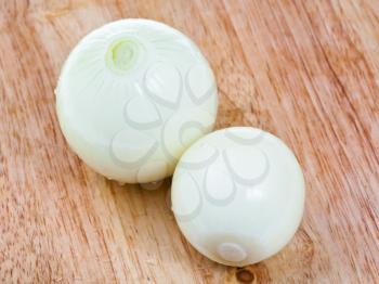 two peeled onions bulbs on wooden board close up