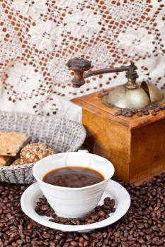 cup of coffee and roasted coffee beans with retro wooden manual mill, biscuit, openwork napkin