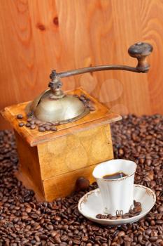 small cup of coffee and roasted coffee beans with retro wooden manual mill and wood wall