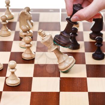 hand with black king overturns white king on chessboard in chess game