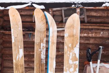 two pairs of wide wooden hunting skis and log house wall in winter day