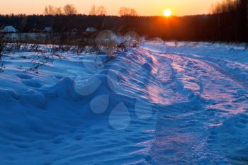 sunset under dark blue winter snowdrifts on country road