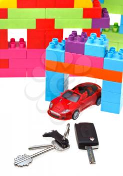 door key, vehicle keys close up, red model car and plastic block house isolated on white background