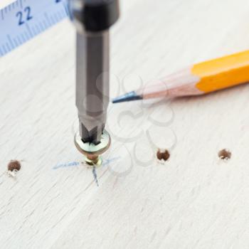measuring tape, pencil and screwdriver wraps screw in wooden plank