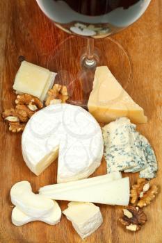glass of red wine and various cheeses on wooden plate close up