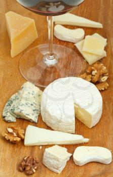 red wine glass and assortment of cheeses on wooden plate close up