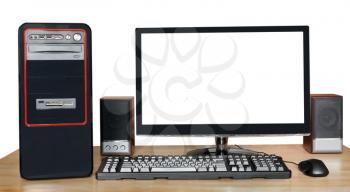 black desktop computer, widescreen display with cutout screen, keyboard, mouse, speakers on wooden table isolated on white background