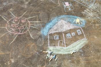 child drawing - house and sun painted on asphalt by colored chalk