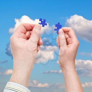 male and female hands with little puzzle pieces with white clouds in blue sky background