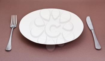 empty white plate with fork and knife on brown background