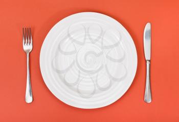top view of empty white plate with fork and knife set on red background