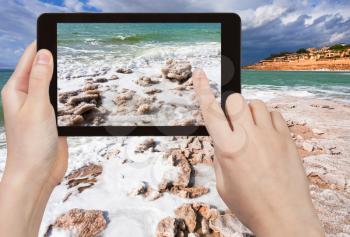 travel concept - tourist taking photo of crystal salt beach on Dead Sea coastline, Jordan on mobile gadget