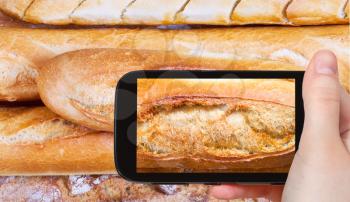 photographing food concept - tourist taking photo of fresh baked loaves of bread on mobile gadget, France