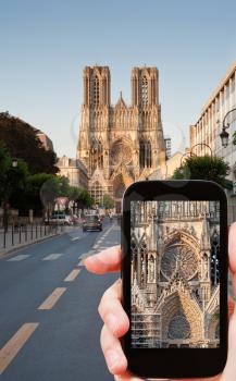 travel concept - tourist taking photo of Reims Cathedral on mobile gadget, France