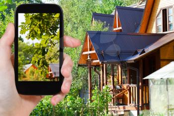 travel concept - tourist takes picture of yard of village house in summer on smartphone