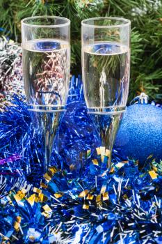 Christmas still life - Two glasses of champagne with blue Xmas decorations on green Christmas tree background