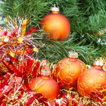 Christmas still life - four orange and yellow Christmas balls, red tinsel on green Xmas tree background