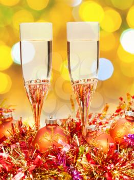 Christmas still life - two glasses of champagne at orange and golden Xmas decorations with yellow and green blurred Christmas lights background