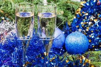 Christmas still life - Two glasses of sparkling wine with blue Xmas balls and tinsel on Christmas tree background