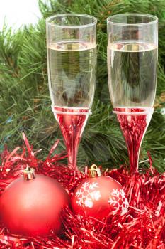 Christmas still life - Two glasses of champagne with red Xmas balls and tinsel on Christmas tree background