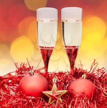Christmas still life - two glasses of champagne at red Xmas decorations with yellow and violet blurred Christmas lights background