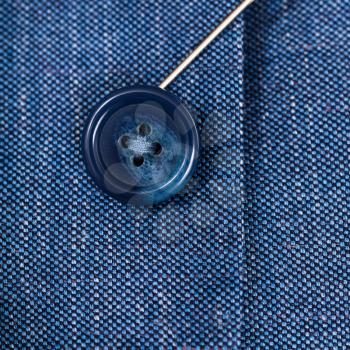 attaching of button to blue silk cloth by needle close up