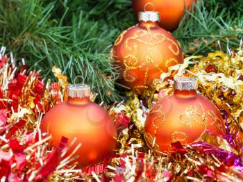 Christmas still life - four orange and yellow Christmas baubles, red tinsel on green Xmas tree background