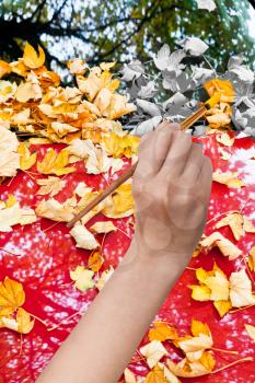 nature concept - hand with paintbrush paints yellow autumn leaves on red car