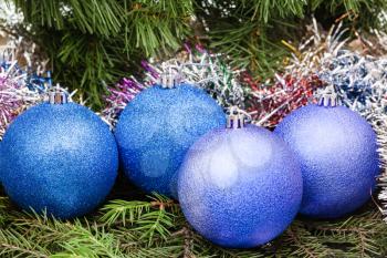 Christmas still life - four blue and violet Christmas balls, tinsel on Xmas tree background