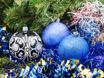 Christmas still life - one black glass and two blue and violet Christmas baubles, tinsel on Xmas tree background