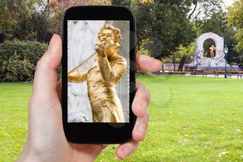 travel concept - tourist snapshot of gilded bronze staue of Waltz King Johann Strauss son in Stadtpark (City Park) in Vienna on smartphone