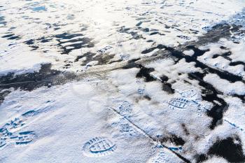 footprints in snow and crack in ice on frozen river in winter