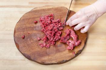 woman cuts meat on wooden cutting board on table