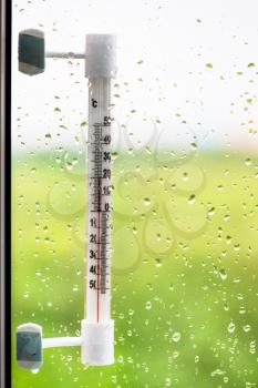 window glass with rain drops and thermometer in summer day