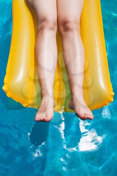 outdoor swimming pool - girl's legs on yellow inflatable mattress in sunny summer day