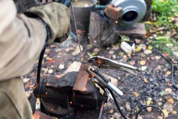 Welder welds iron ring by point electric welding in outdoor rural workshop